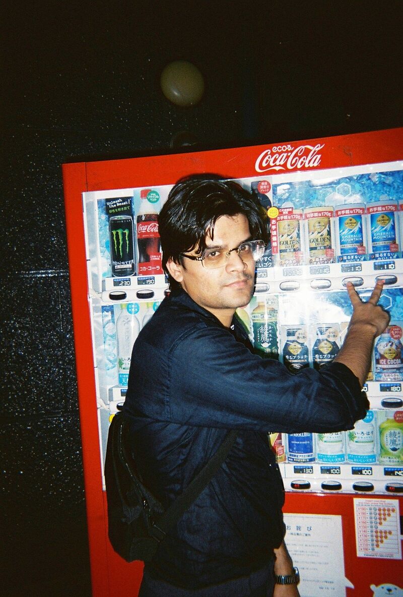 Arpit making a peace sign in front of a red Coca-Cola vending machine at night in Japan